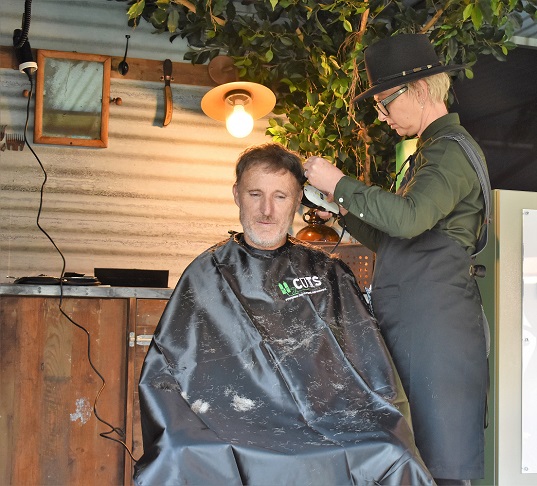 man sitting in barber chair receiving haircut from hairdresser in hat