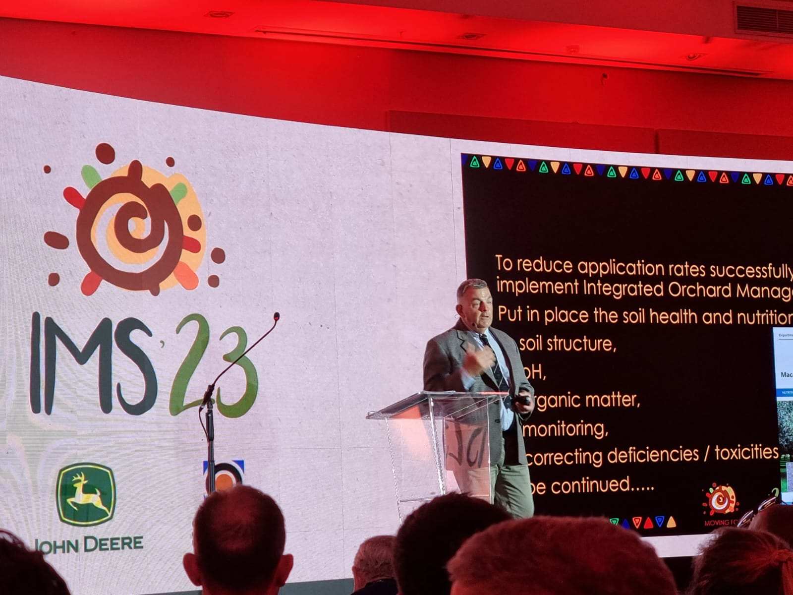 Man in suit on stage addressing audience with IMS 23 logo in the background