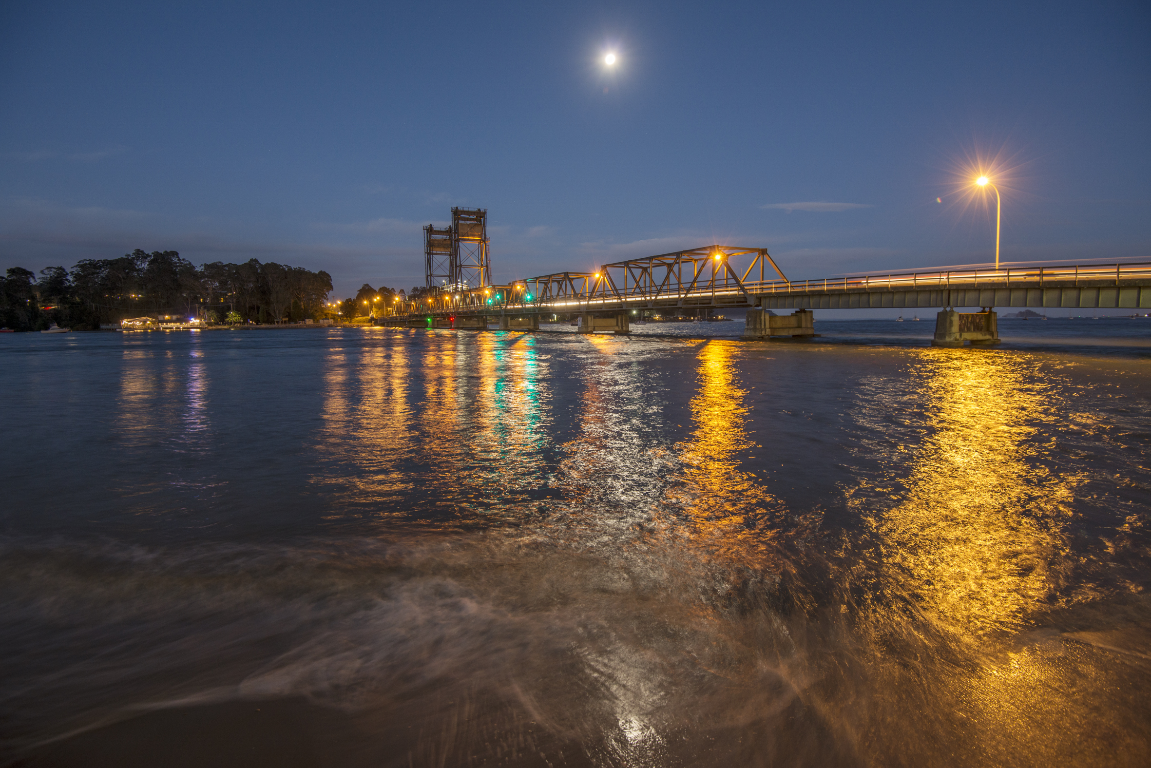 An evening photo from the back of a boat looking towards a bridge