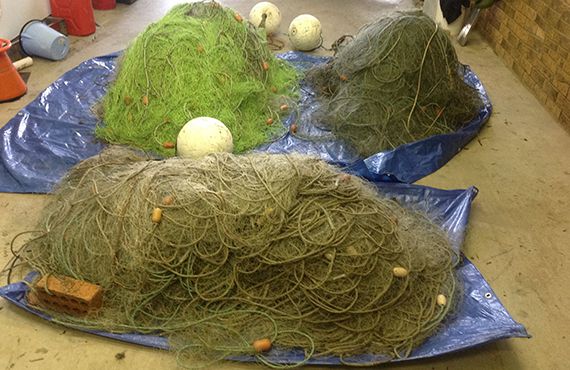 Three piles of seized mesh nets on sitting on tarpaulins on the ground