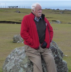 Tony leaning against a large rock with and wearing a coat and gloves