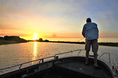 A fisherman is holding his rod on the bow of a boat at sunset