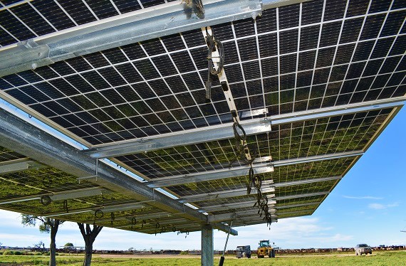 Under side close up of solar panels  on farm paddock with tractor and farm vehicles in background