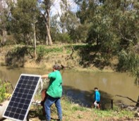person holding solar panel next to riverbank