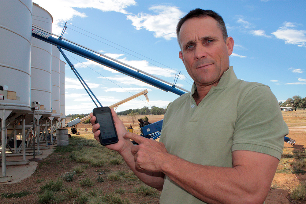 Geoff Casburn displaying the app, standing by a row of silos.