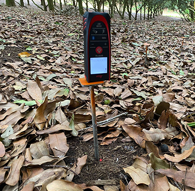 square device inserted into soil, surrounded by leaves on the ground 