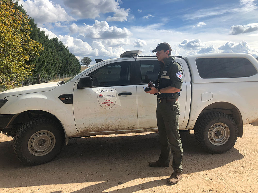 A game licensing inspector stands beside his patrol car